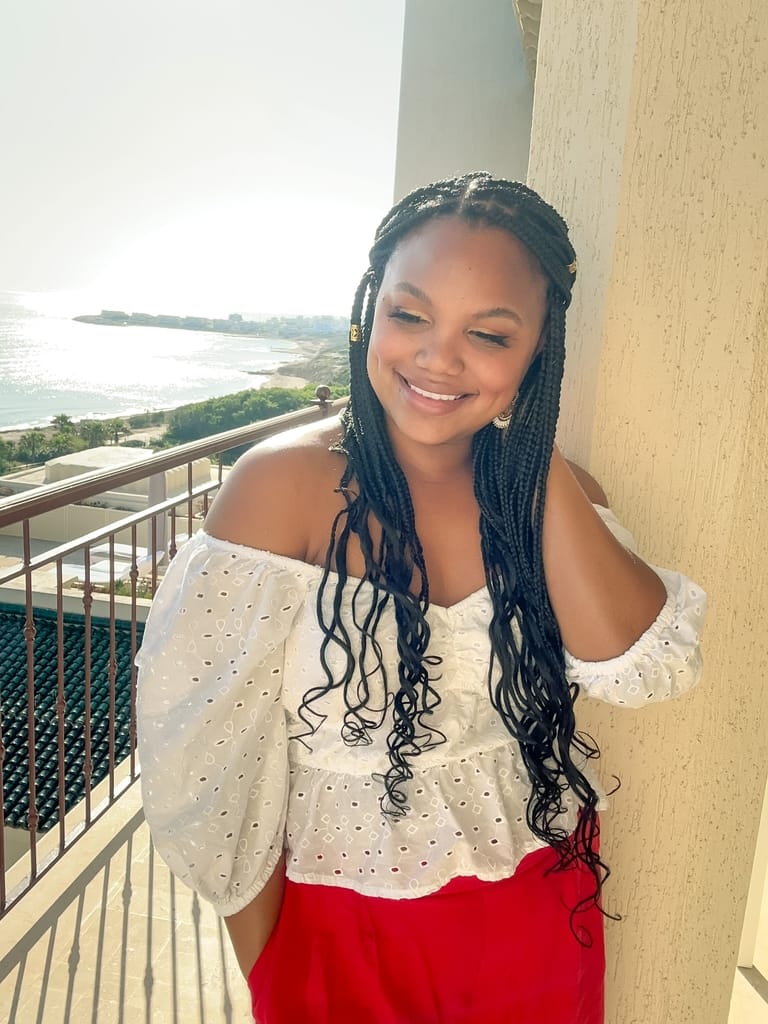 girl with braids, wearing white top and red pants, smiling