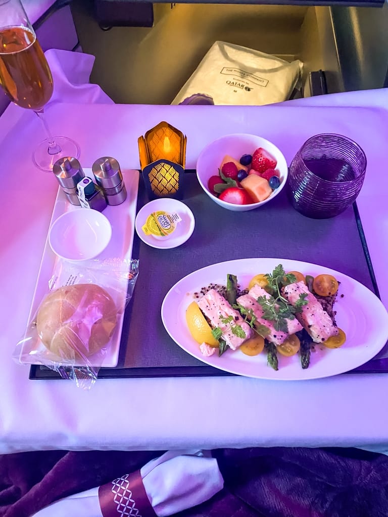 Dinner being served on glass plate with a candle, fruit, and bread on Qatar Airways Business class